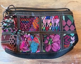 Pode incluir: Uma clutch retangular multicolorida com acabamento e zíper em couro preto. A clutch apresenta painéis bordados com desenhos geométricos e florais em tons de rosa, azul, laranja e verde. Um pendão de contas pende do zíper.