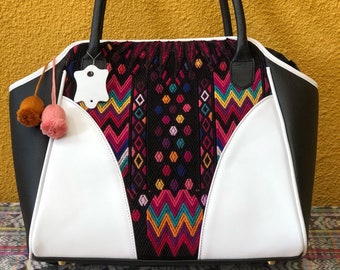Pode incluir: Bolsa tote de couro preto e branco com um painel bordado colorido com padrões geométricos. A bolsa tem duas alças pretas e uma guarnição de couro branco.