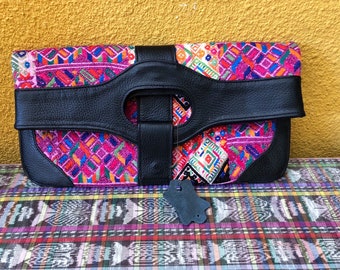 May include: A black leather clutch with a large, circular cutout and a flap closure. The clutch is decorated with a colorful, geometric pattern.