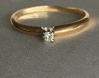 Könnte beinhalten: Ein einfacher Goldring mit einem kleinen Diamanten in der Mitte.