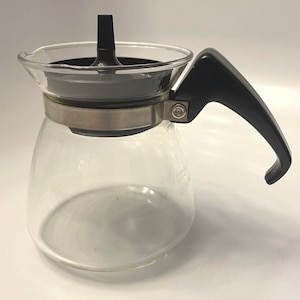 May include: A clear glass coffee maker with a black handle and lid. The coffee maker has a stainless steel band around the middle and a spout for pouring. The design is simple and functional, suitable for brewing coffee.