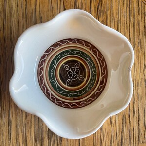 May include: White ceramic bowl with a scalloped edge and a brown, green, and white floral design in the center.