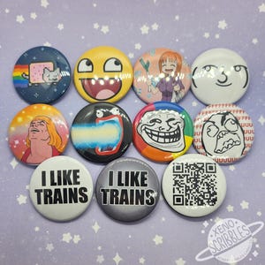 Puede incluir: Una colección de botones redondos con varios diseños. Los botones presentan memes, personajes de dibujos animados y texto, incluyendo "I LIKE TRAINS" y un código QR. Los colores incluyen azul, amarillo, naranja y blanco.