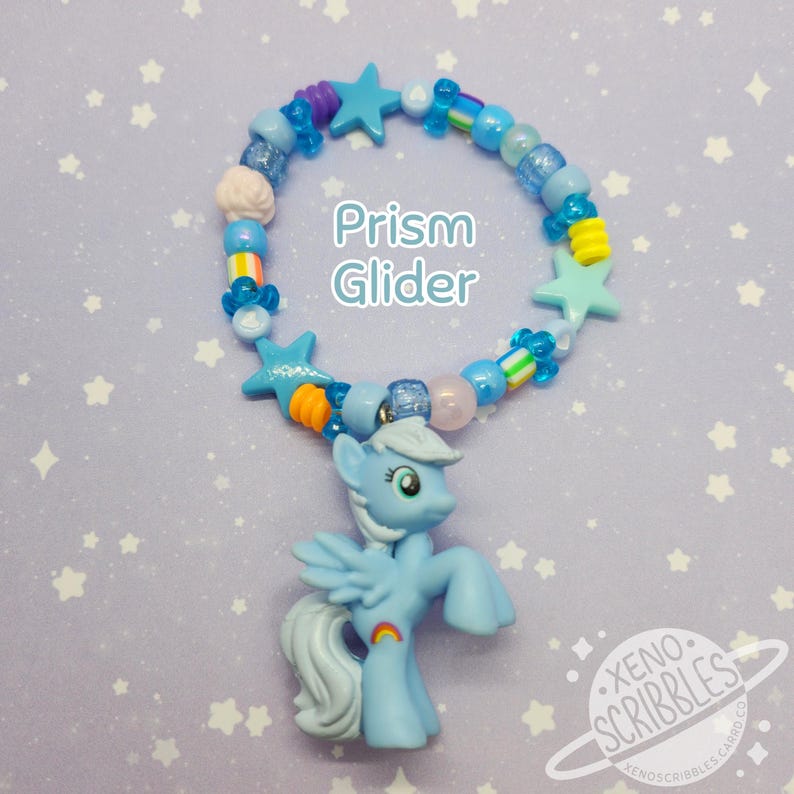 May include: A blue beaded bracelet with a rainbow charm and a blue pony charm. The bracelet has blue, white, and yellow stars and beads. The text "Prism Glider" is written on the bracelet.