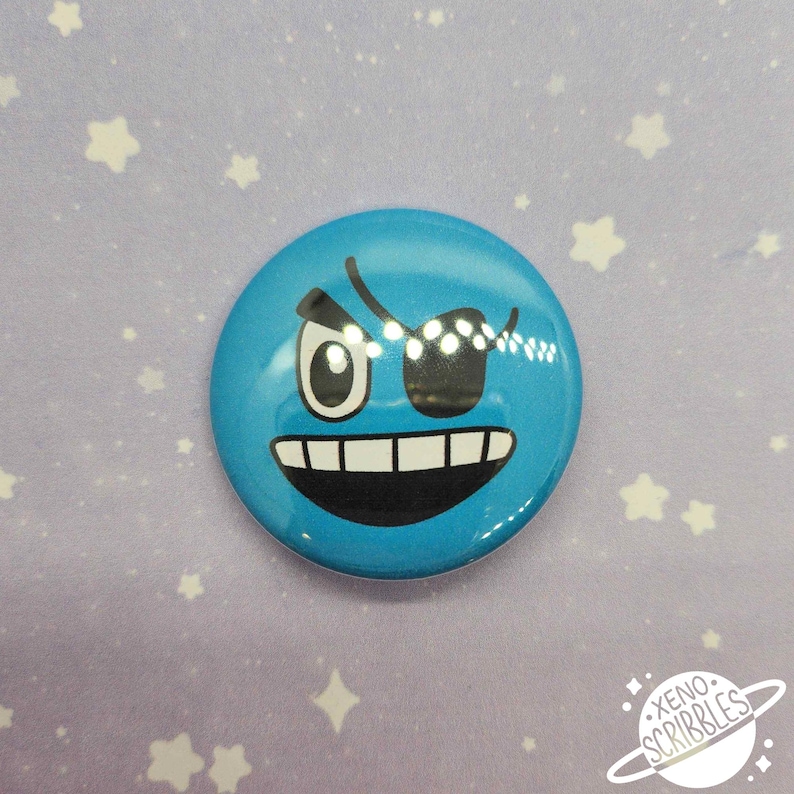 May include: Blue button with a cartoon face with one eye and an eyepatch. The face is winking and has a mischievous expression.