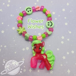 May include: A pink and green beaded bracelet with a charm of a red pony with green hair. The bracelet has green flowers, hearts, and smiley faces. The text "Flower Wishes" is written on the image.