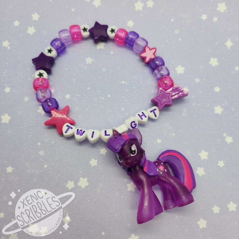 May include: A purple and pink beaded bracelet with a star charm and a small purple Twilight Sparkle pony figure. The bracelet spells out "TWILIGHT" in white letters.