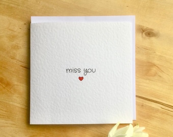 Puede incluir: Una tarjeta blanca con el texto "miss you" en letras negras y un pequeño corazón rojo.