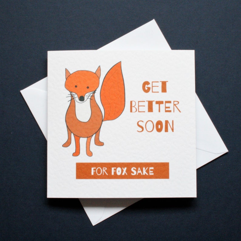 Pode incluir: Cart&atilde;o de felicita&ccedil;&otilde;es quadrado com uma ilustra&ccedil;&atilde;o de uma raposa laranja e o texto "Get Better Soon" e "For Fox Sake" em laranja. O cart&atilde;o est&aacute; sobre um envelope branco, sobre um fundo escuro.