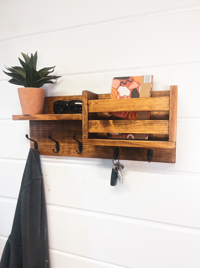 coat rack with hooks for keys, coats and hats. Features a shelf and a pocket for mail .