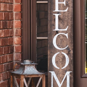 Welcome sign for front porch, brown in color, roman font with wreath accents at top and bottom