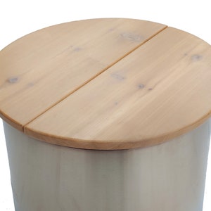 May include: A light-coloured wooden lid with a rounded edge sits atop a cylindrical container. The lid is made of two wooden pieces joined together. The container has a light, neutral colour.