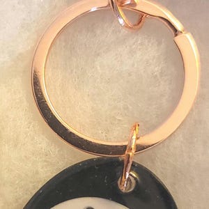 May include: Rose gold keychain with a lobster clasp and a round key ring. A black and white tag is attached, featuring the text "Ander Berry Bracelets EST. 2014".