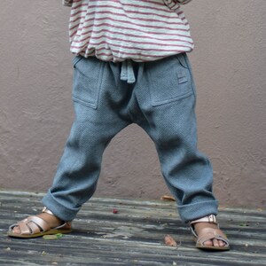 May include: Gray toddler pants with a drawstring waist and two front pockets. The pants are paired with a striped shirt and gold sandals. The pants have a relaxed fit and cuffed hems.