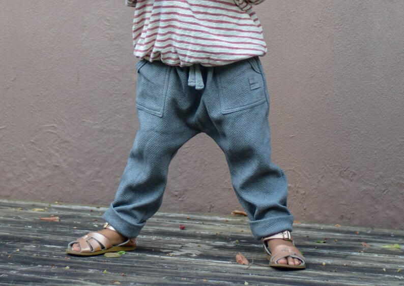 May include: Gray toddler pants with a drawstring waist and two front pockets. The pants are paired with a striped shirt and gold sandals. The pants have a relaxed fit and cuffed hems.