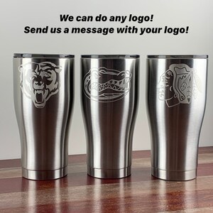 May include: Three stainless steel tumblers with different logos engraved on them. The logos are a bear, an alligator, and a hockey team logo. The text "We can do any logo! Send us a message with your logo!" is visible at the top of the image.