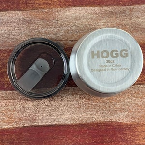 May include: A silver lid for a 30oz tumbler with the text "HOGG 30oz Made in China Designed in New Jersey" engraved on the top.