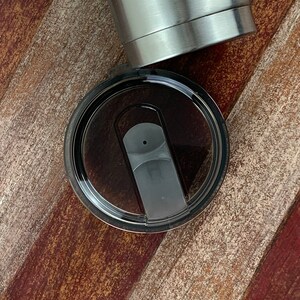 May include: A black lid with a clear plastic insert and a black slider for a stainless steel tumbler.