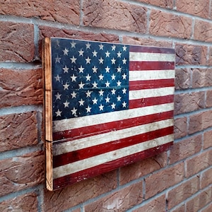 May include: A distressed wooden American flag with red, white, and blue stripes and a field of blue stars. The flag is mounted on a brick wall.
