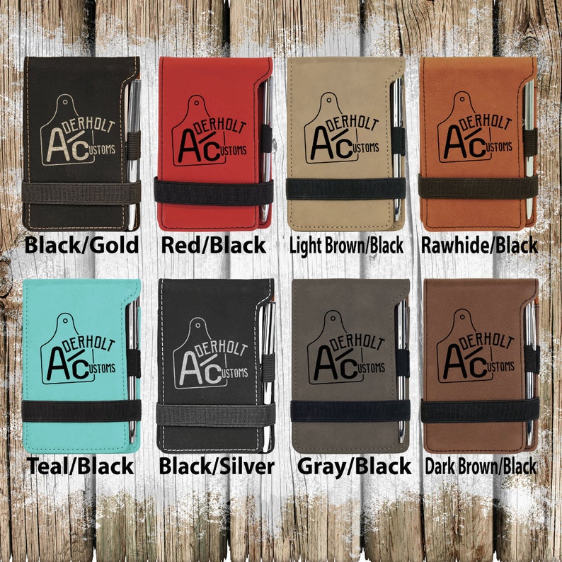 Puede incluir: Ocho combinaciones de colores diferentes de una libreta de cuero sint&eacute;tico con un bol&iacute;grafo adjunto. La libreta tiene un logotipo en blanco y negro que dice "Derholt Customs" con una "A" estilizada y un dise&ntilde;o de etiqueta de ganado. Los colores son negro/oro, rojo/negro, marr&oacute;n claro/negro, cuero crudo/negro, azul verdoso/negro, negro/plata, gris/negro y marr&oacute;n oscuro/negro.
