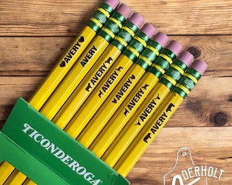 May include: A pack of yellow pencils with green and white stripes. Each pencil is personalized with the name "Avery" and a different design. The pencils are packaged in a green and white box with the brand name "Ticonderoga" printed on it.