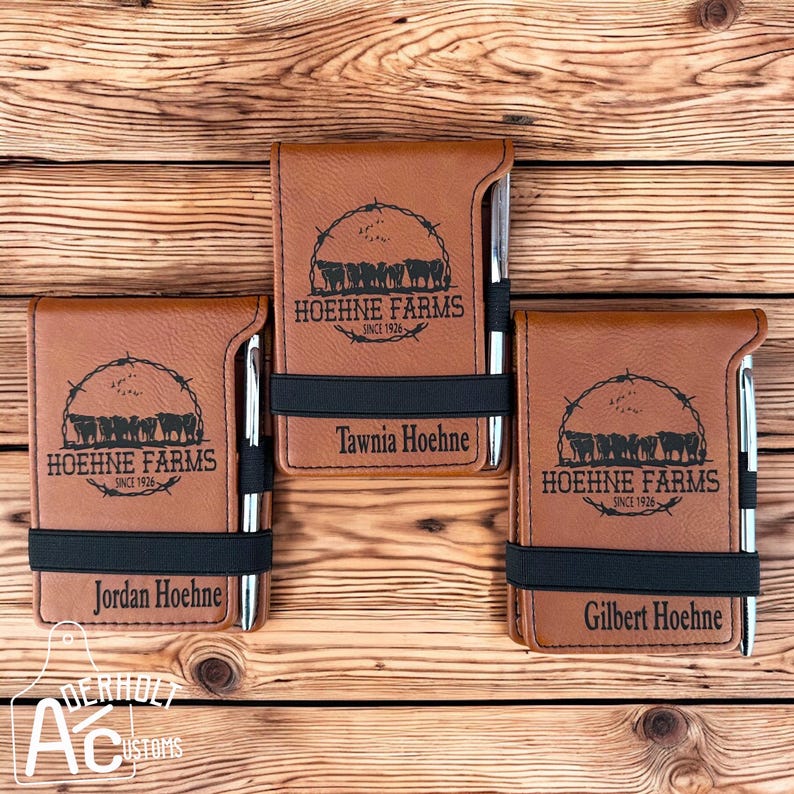 Puede incluir: Tres cuadernos de cuero marr&oacute;n con bandas el&aacute;sticas negras y bol&iacute;grafos. Cada cuaderno tiene un logotipo en blanco y negro con el texto "HOEHNE FARMS SINCE 1926" y un c&iacute;rculo de vacas. Cada cuaderno est&aacute; personalizado con un nombre: "Jordan Hoehne", "Tawnia Hoehne" y "Gilbert Hoehne".