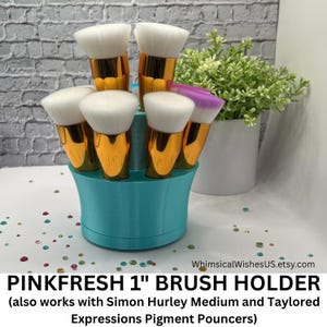 May include: A collection of makeup brushes with white bristles and gold handles are displayed in a turquoise brush holder. The text "PINKFRESH 1" BRUSH HOLDER" is visible at the bottom of the image. The brush holder is approximately 1 inch in diameter.