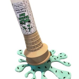 Może przedstawiać: Nowatorski klej w sztyfcie z białą nasadką i etykietą z napisem "Beardy Art Precision Craft Glue 59 mL". Klej w sztyfcie umieszczony jest w brązowym rożku do lod&oacute;w, kt&oacute;ry umieszczony jest na jasnoniebieskiej, stopionej bazie przypominającej lody z czarnymi posypkami.