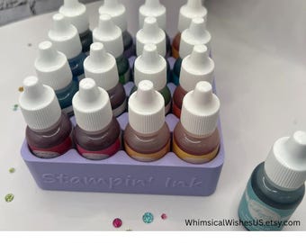 May include: A light purple ink storage tray filled with small ink bottles with white caps. The bottles contain various colors of ink. The text "Stampin' Ink" is embossed on the tray. The text "REINKER STORAGE" is at the bottom.