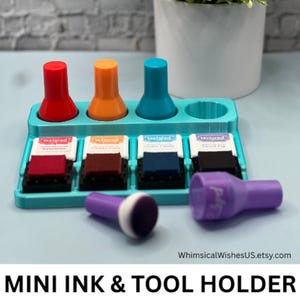 May include: A teal mini ink and tool holder with four colored ink pads and four matching ink daubers. The holder has slots for the ink pads and daubers. The ink pads are red, brown, blue, and black. The daubers are red, orange, blue, and purple.