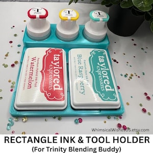 May include: A teal rectangle ink and tool holder with three white stampers with red, yellow, and teal tops. Two ink pads are visible, one red and one teal, with the text "taylored expressions". The text "Watermelon" and "Blue Raspberry" are also visible.