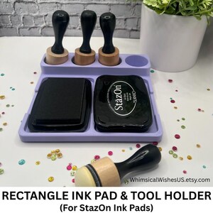 May include: A lavender rectangle ink pad and tool holder with three black handled stampers and two black ink pads. One ink pad is labeled "StazOn". The holder also has a small round compartment. The text "RECTANGLE INK PAD & TOOL HOLDER" is at the bottom.