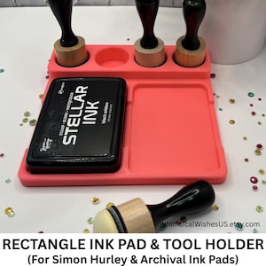May include: A coral-colored rectangle ink pad and tool holder with three tool slots and a rectangular ink pad slot. A black ink pad labeled "STELLAR INK" sits in the holder. The holder also has a small ink blending tool.