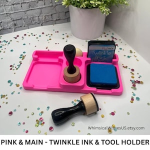 May include: A bright pink ink and tool holder with a black and blue ink pad, a black handled ink applicator, and a blue ink pad. The text "Twinkle Inks" is visible on the ink pad.