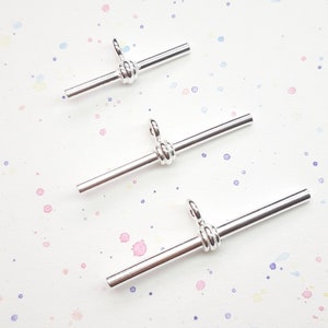 May include: Three silver metal connector pieces for jewellery making. Each piece has a loop on one end and a twisted wire design in the middle.
