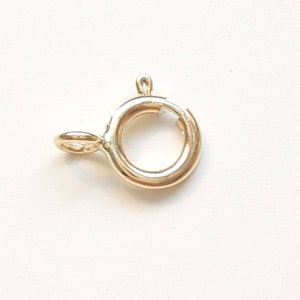 May include: Gold-toned metal clasp with a round ring and a small loop. The clasp is designed to be used for attaching jewellery or other items.