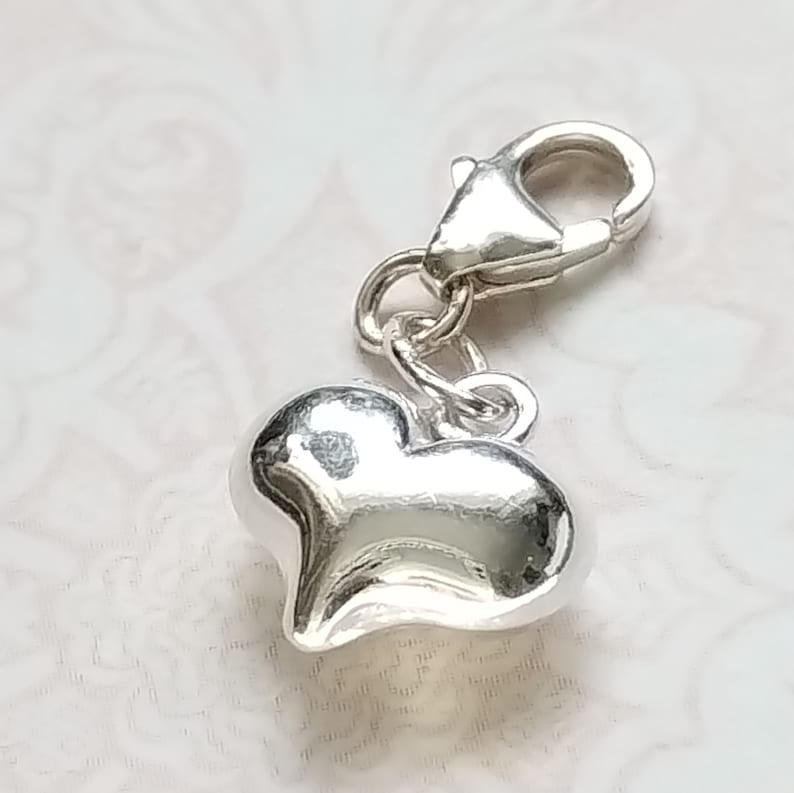 May include: A silver charm with a heart-shaped pendant and a lobster clasp.