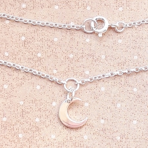 May include: A silver chain necklace with a crescent moon charm. The chain is delicate and the charm is small and simple.