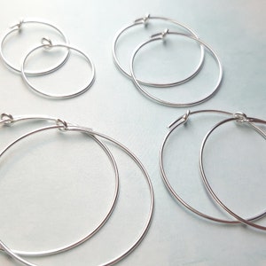 May include: Four silver hoop earrings of varying sizes. The hoops are simple and elegant, with a smooth finish.