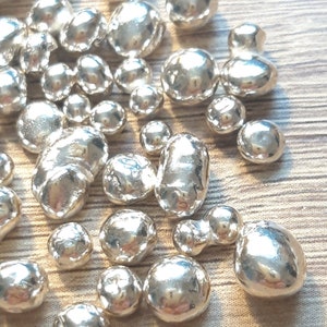 K&ouml;nnte beinhalten: Nahaufnahme eines Haufens silberfarbener Metallk&uuml;gelchen. Die K&uuml;gelchen sind glatt und rund und in einem zuf&auml;lligen Muster angeordnet.