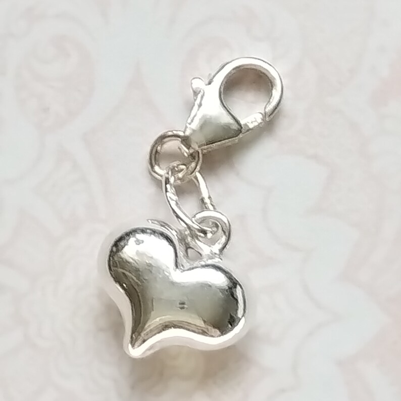 May include: A silver charm with a heart-shaped pendant. The charm has a lobster clasp.