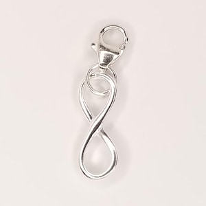 May include: A silver infinity charm with a lobster clasp. The charm is shaped like the infinity symbol, with a loop at the top for attaching to a chain or bracelet. The clasp is a standard lobster claw style.