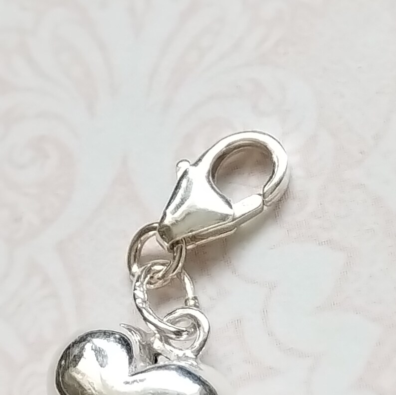 May include: Silver charm with a heart shape and a lobster clasp.