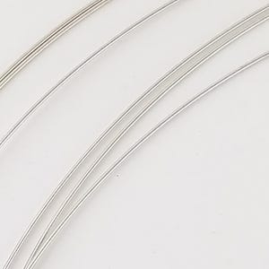 May include: Five spools of silver wire, varying in thickness, are arranged in a curved pattern on a white background.
