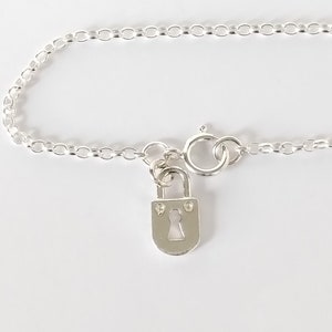 May include: A silver chain bracelet with a small padlock charm. The padlock has a keyhole and two small decorative accents.