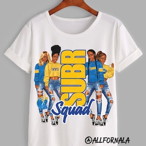 May include: White t-shirt with a graphic of four women wearing blue and yellow clothing. The text "SUBR Squad" is printed on the shirt.