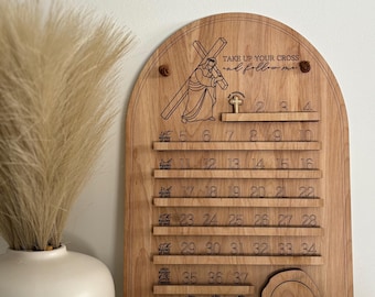 May include: Wooden wall hanging with an arched top, featuring the text "TAKE UP YOUR CROSS and follow me." It has rows of numbered slots and an illustration of a person carrying a cross. The numbers 1-40 are displayed. A decorative piece.