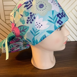 Light flowers on blue background scrub cap. With choice of European or ponytail. Button add on available.
