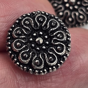 May include: Silver-toned buttons with a decorative, intricate design. The buttons have a raised, circular pattern with a central dot.