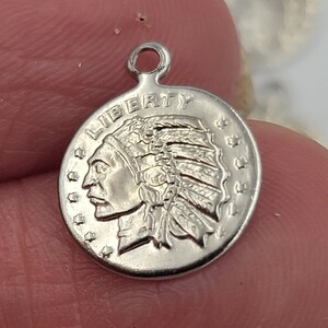 May include: Silver charm featuring a profile of a Native American wearing a headdress. The charm is round and has the word "LIBERTY" inscribed around the edge.